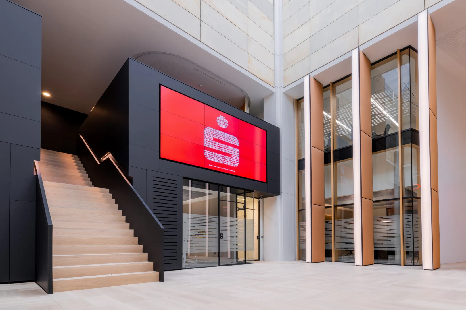 Kundenhalle mit einer Treppe und einem großen Bildschirm mit dem Logo der Sparkasse